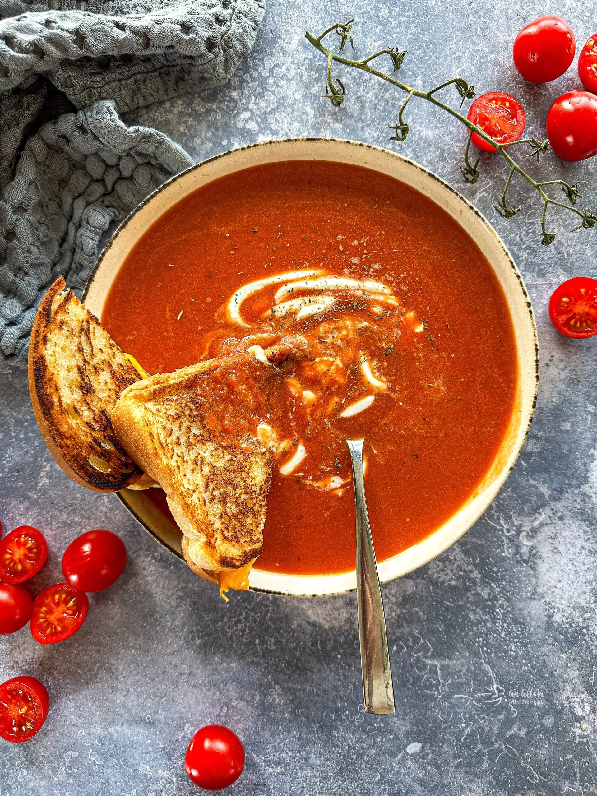 Fire Roasted Tomato soup with a grilled cheese sandwich halved and a spoon in a white bowl.