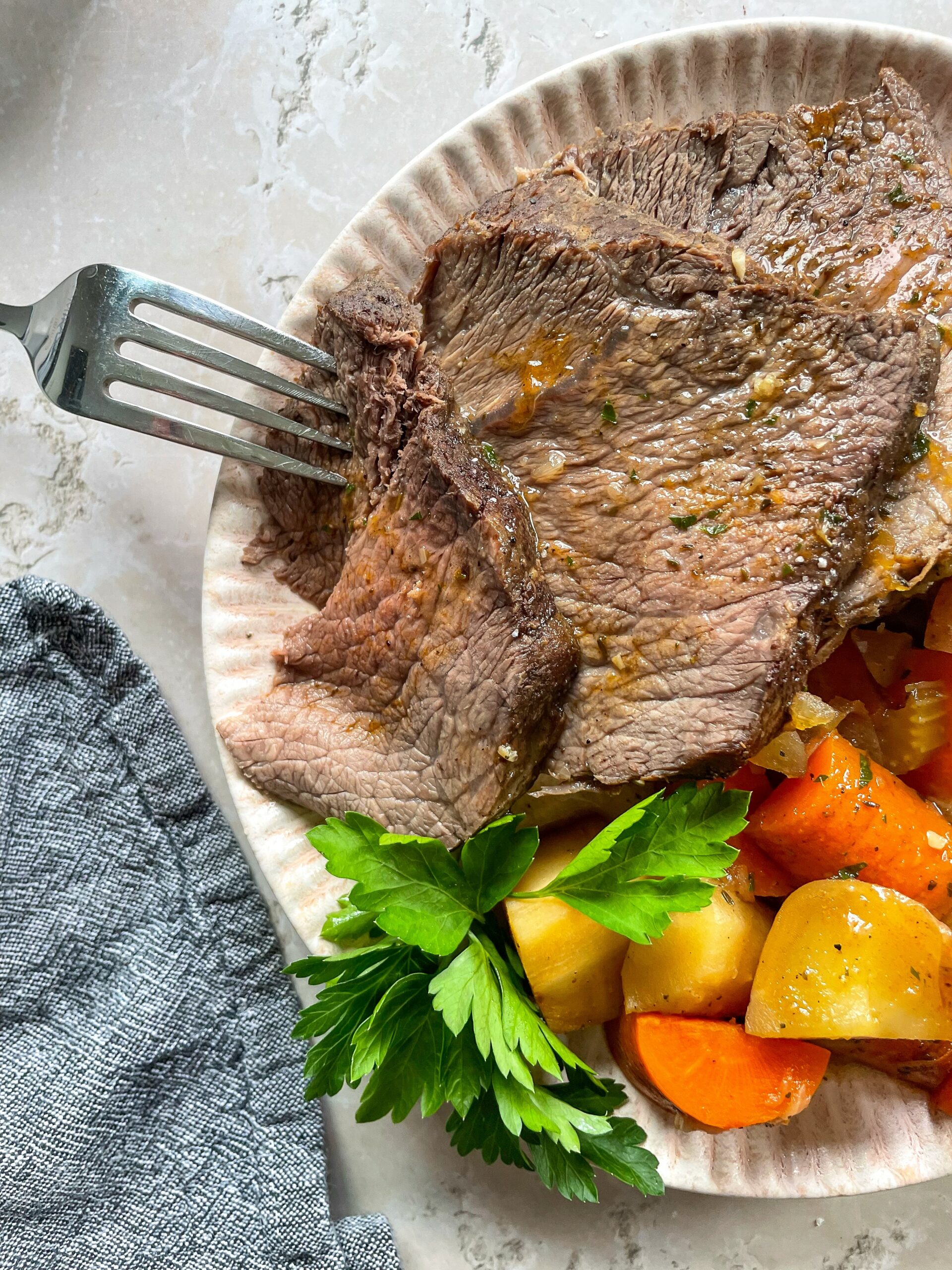 close up of copycat Bob Evans pot roast sliced with a fork in one piece on a cream colored scalloped plate.