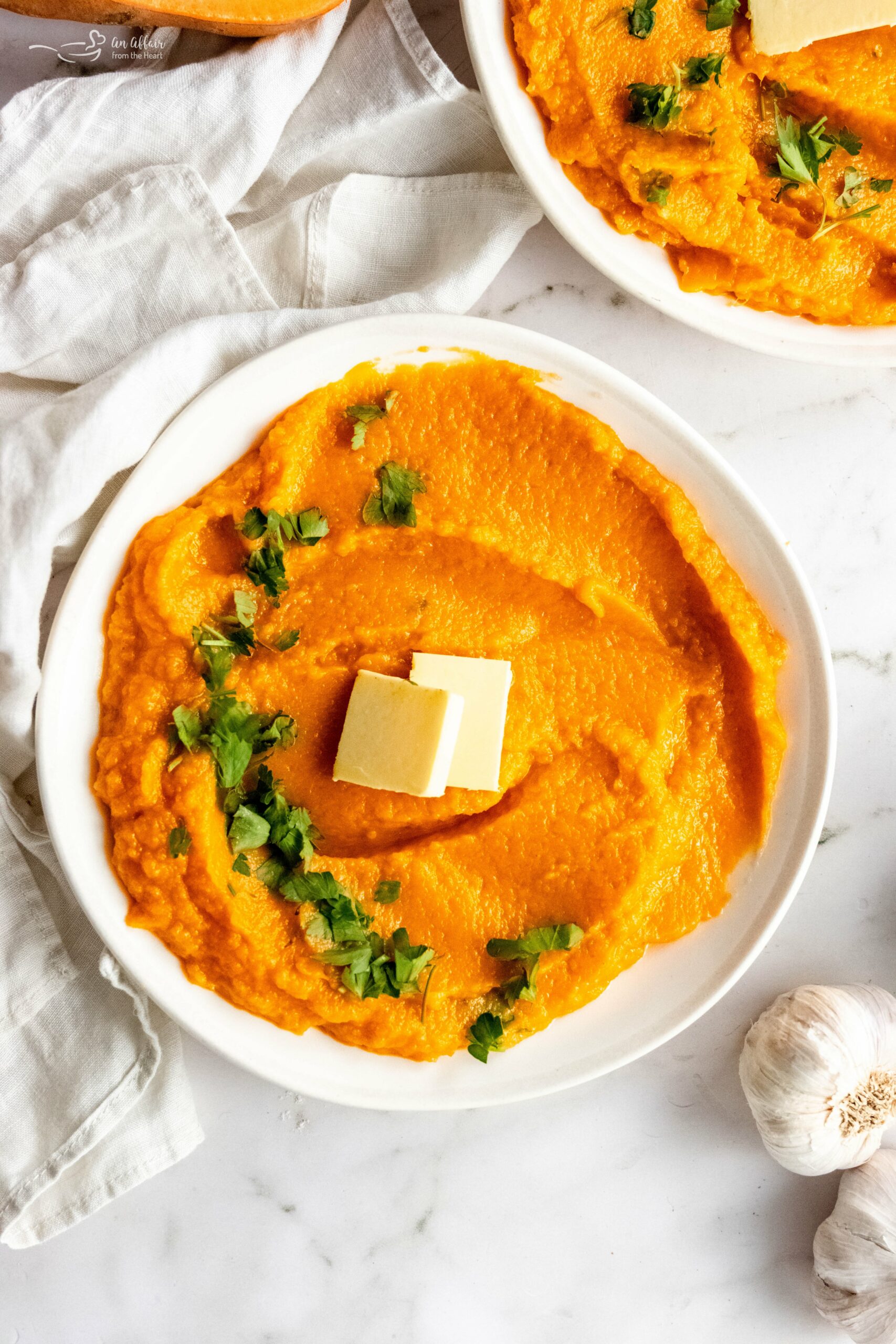 Instant Pot Sweet Potato Mash topped with parsley and butter in a white serving bowl